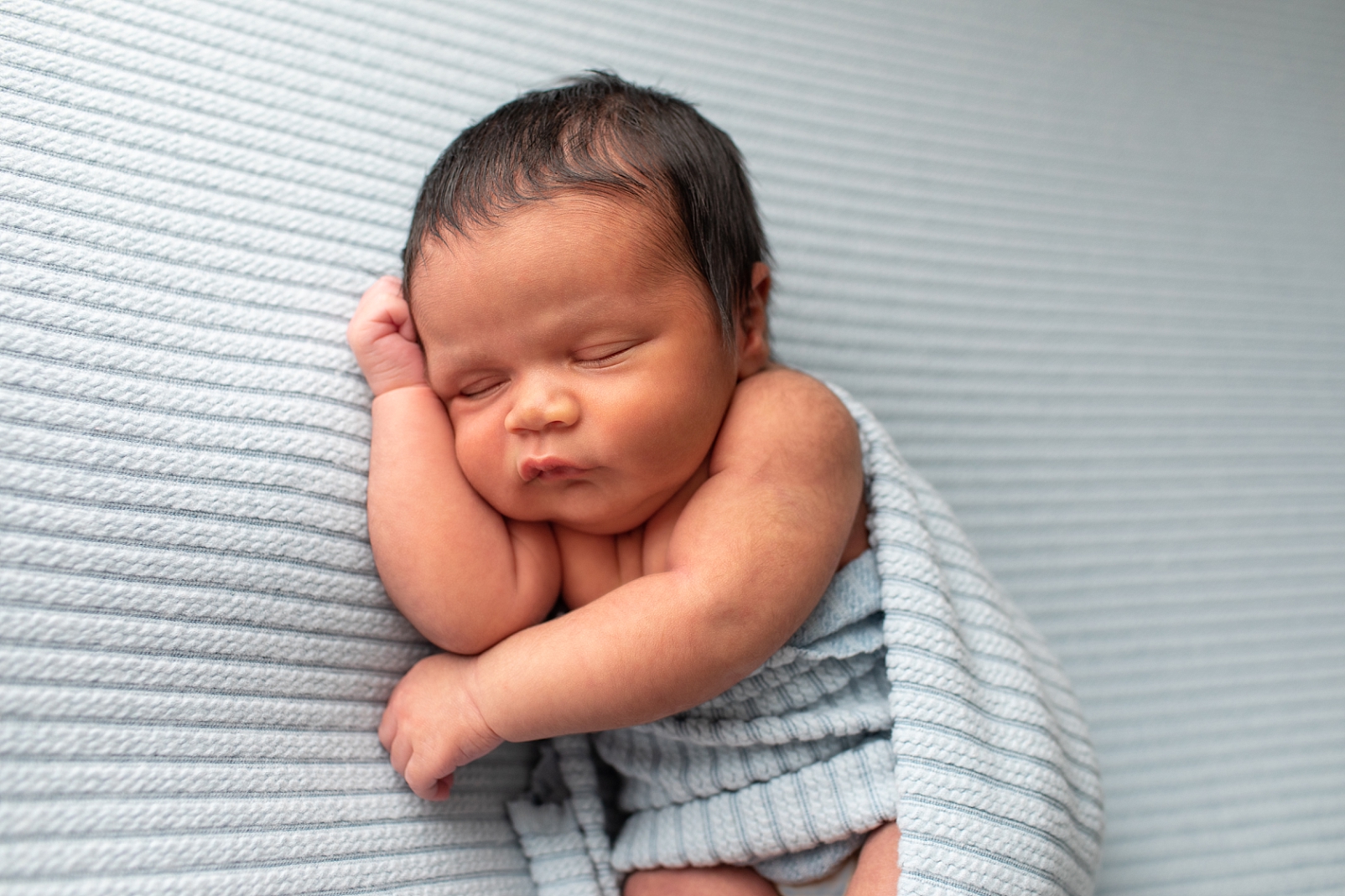 Newborn boy in tummy lying pose on ribbed light blue fabric