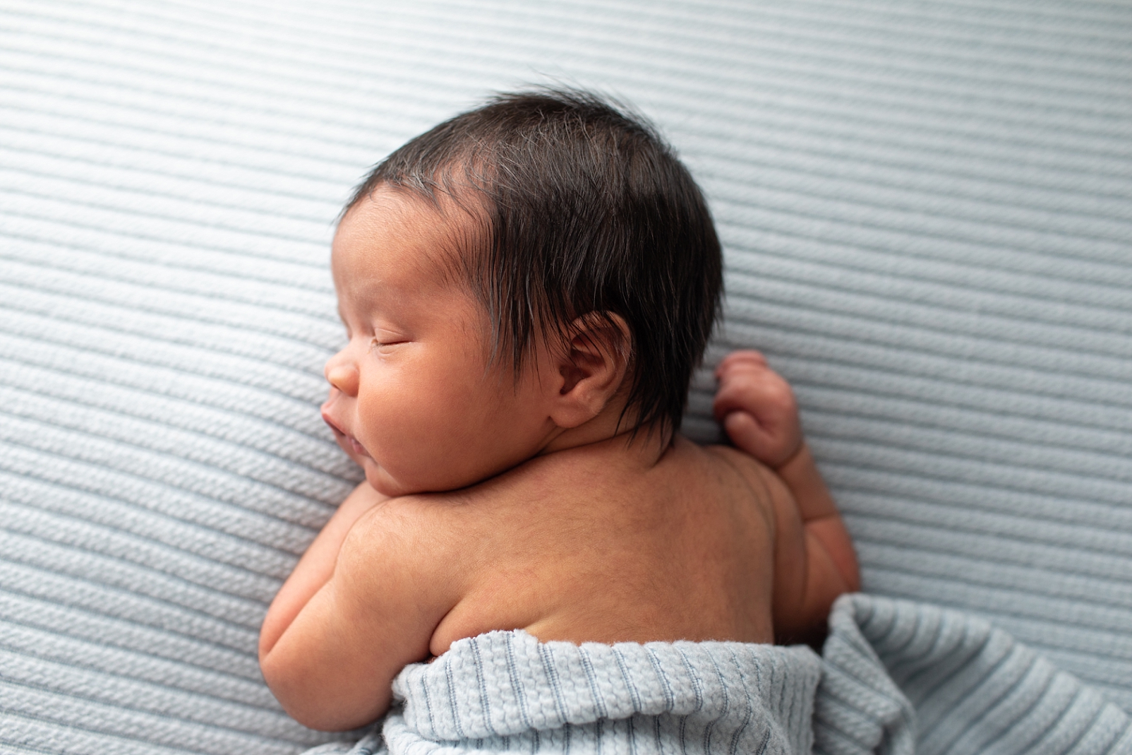 Newborn boy in tummy lying pose on ribbed light blue fabric