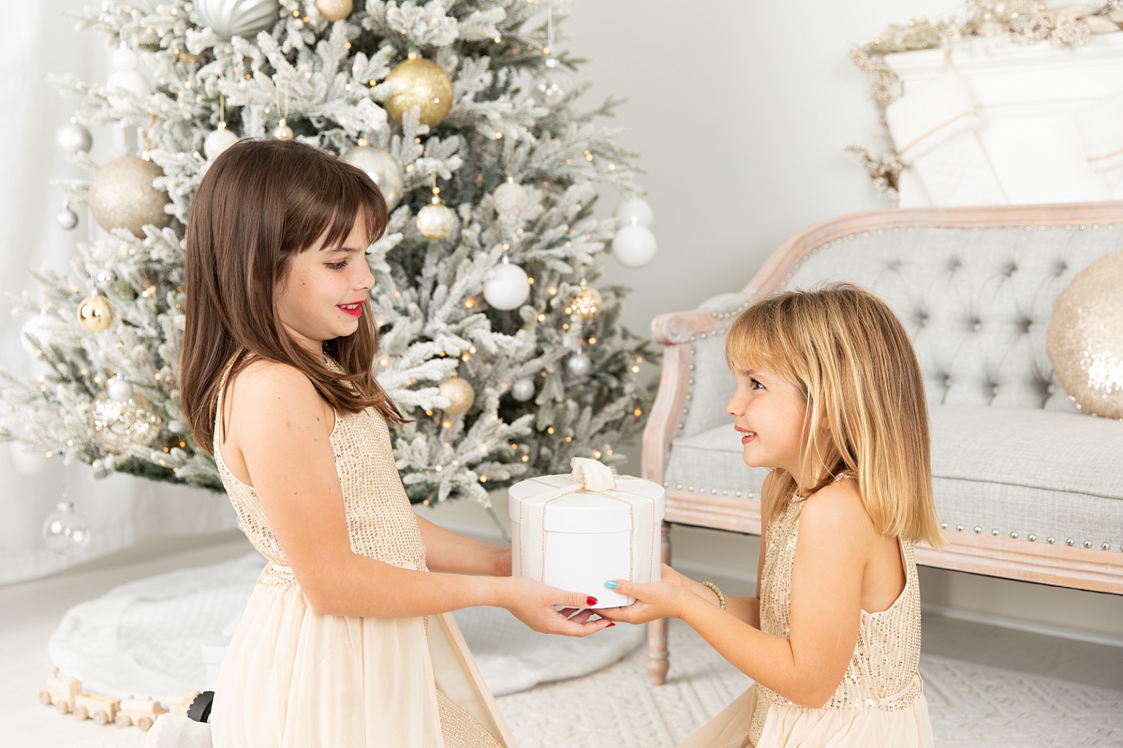 2 Sisters holding a present in front of a flocked Christmas tree
