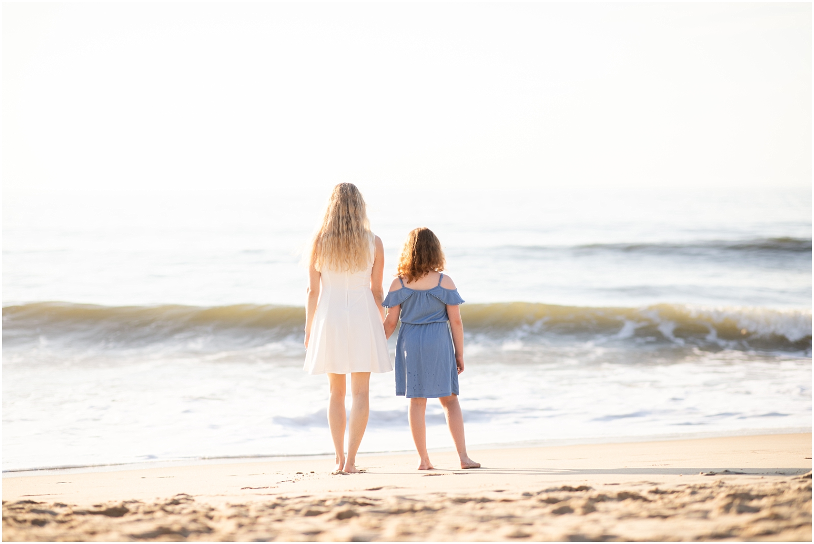 A mother and daughter are standing with backs to the camera while looking out at the ocean - Rebecca Leigh Photography