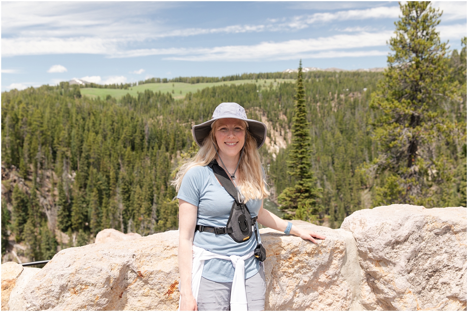 A photo of a lady wearing a hat and blue shirt standing in front of a rock wall in Yellowstone National Park, taken using a tripod by Rebecca Leigh Photography
