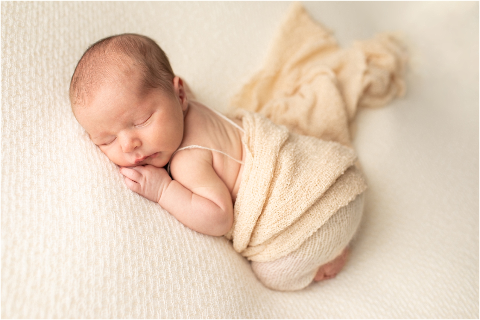 Newborn baby boy wrapped in a cream color swaddle sleeping