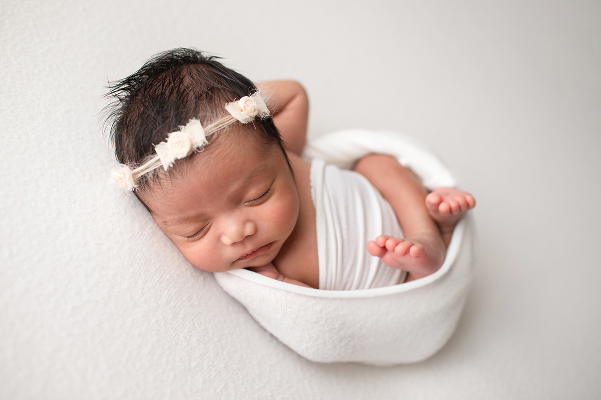 newborn girl wrapped in white fabric with peach bow headband