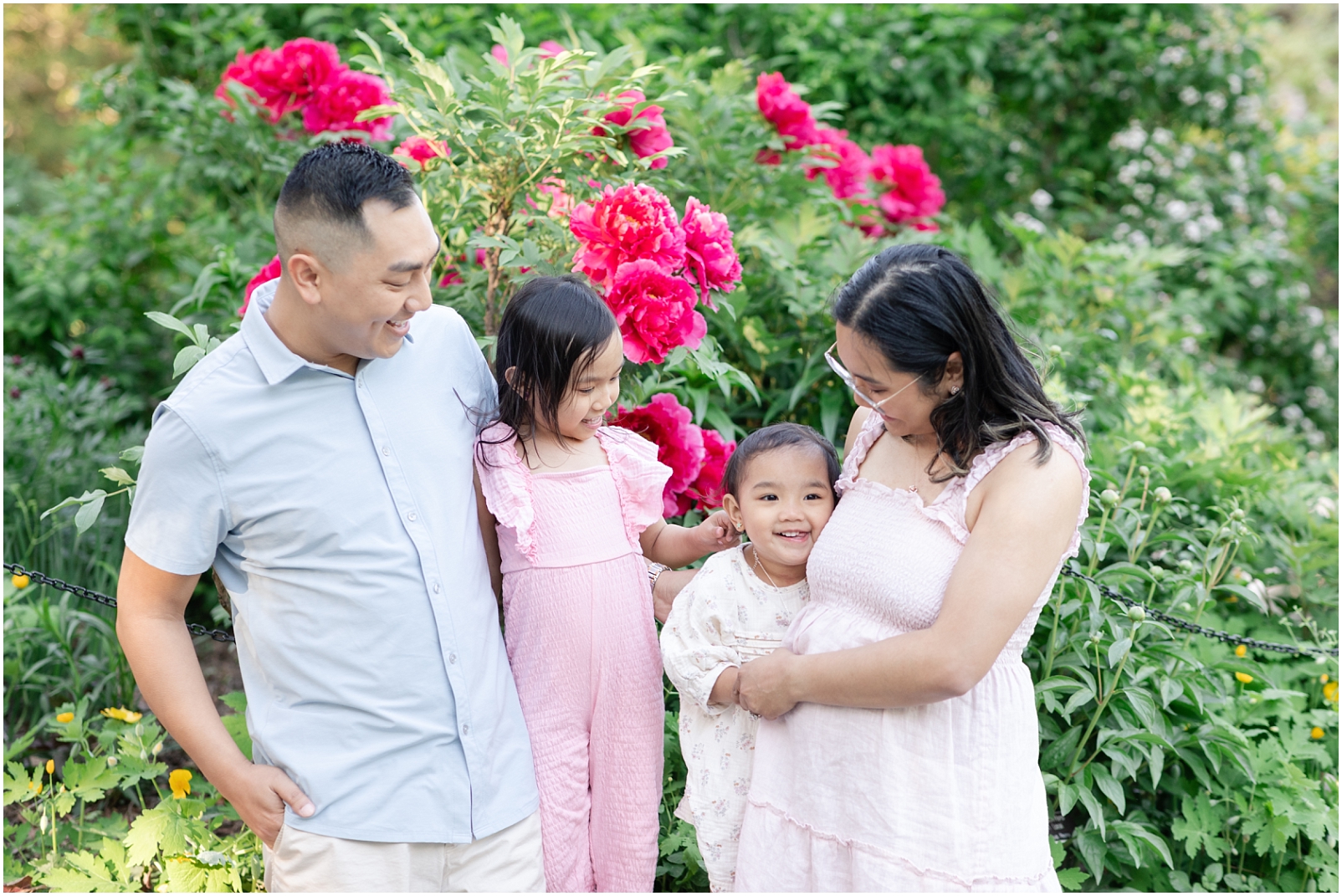 Family of 4 standing in front of fuchsia flowers and smiling at each other
