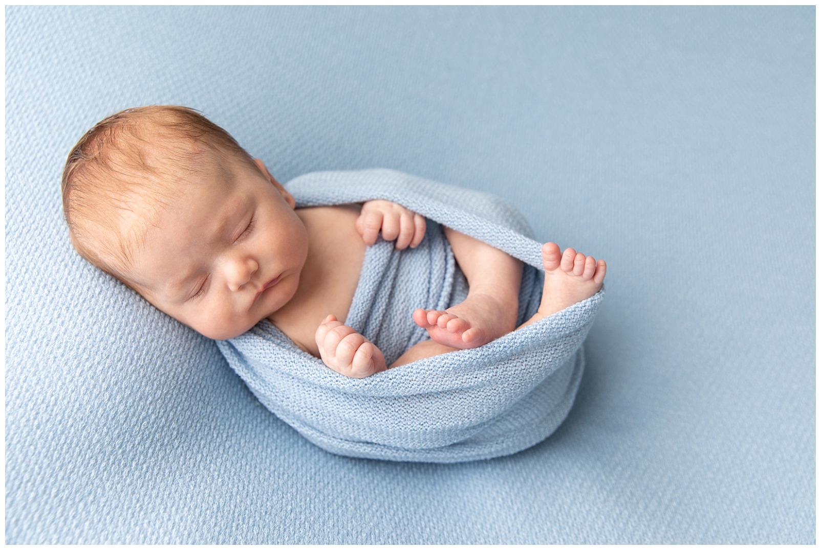 Newborn boy wrapped in blue fabric and sleeping