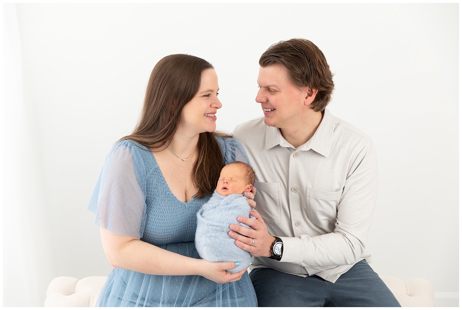 A couple smiling at eachother and holding their newborn baby boy wrapped in blue