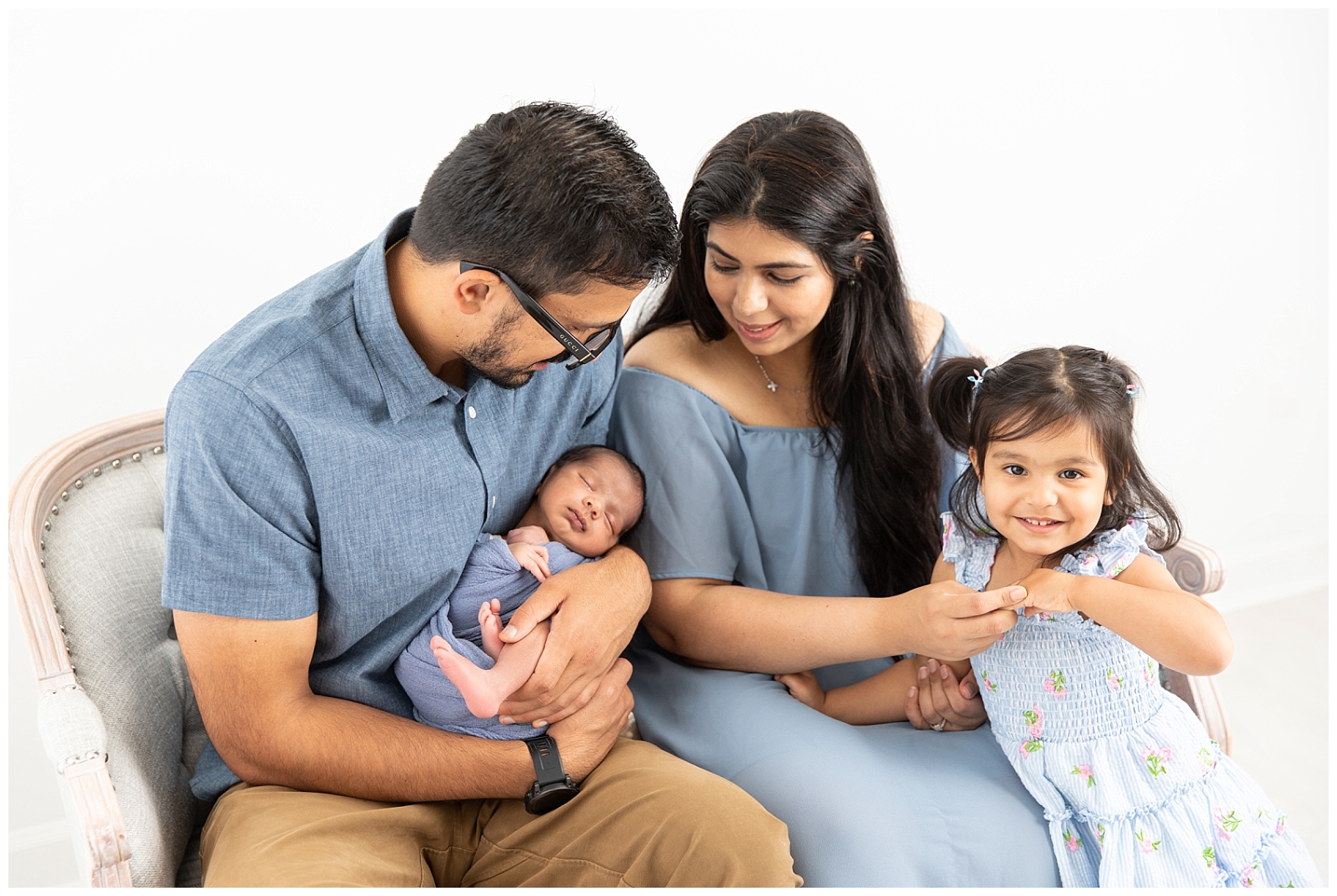 A family of four wearing shades of blue and looking at their newborn baby boy