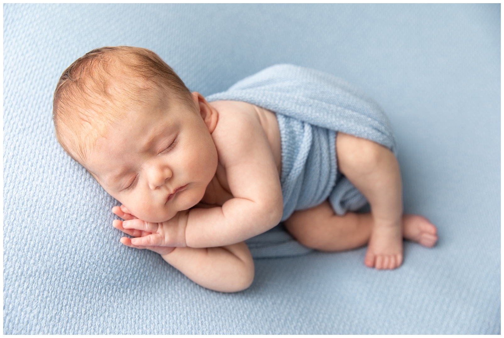 5 tips to prepare for a newborn photo session to photograph a Newborn boy with hands posed together on a textured light blue blanket