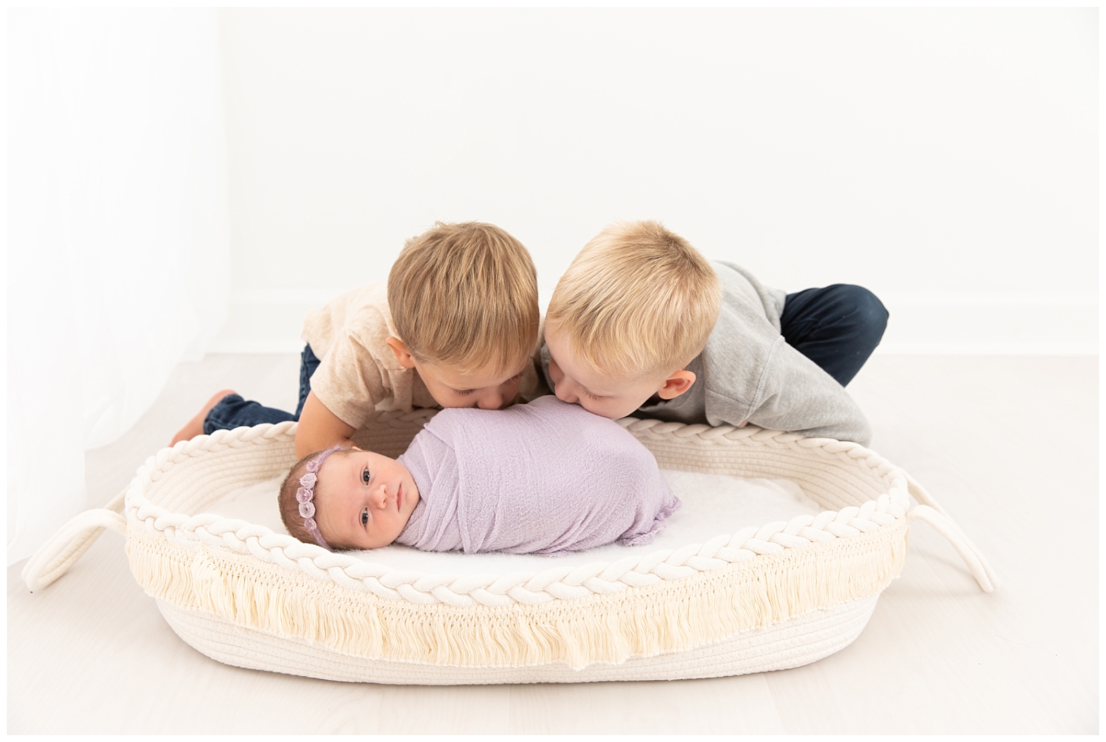 5 tips to prepare for a newborn photo session with a toddler and an older brother leaning towards their baby sister wrapped in lavender and a floral headband