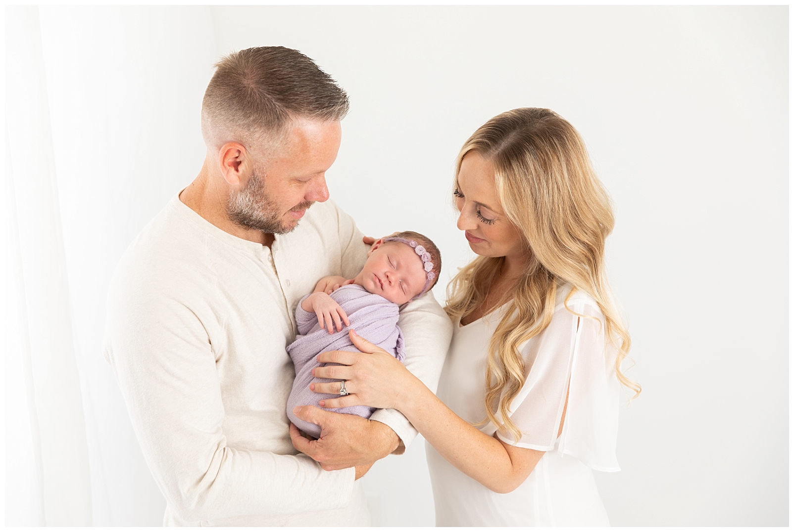 A couple dressed in white holding their newborn baby girl